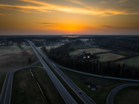 Aerial view of the highway intersection between the A5 and A8 roads at sunset, with golden light over the rural landscape and fields in Olaine parish, Olaine Municipality, Latvia.