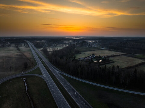 Aerial view of the A5 and A8 highway intersection at sunset with surrounding forests and fields in Olaine parish, Olaine Municipality, Latvia.