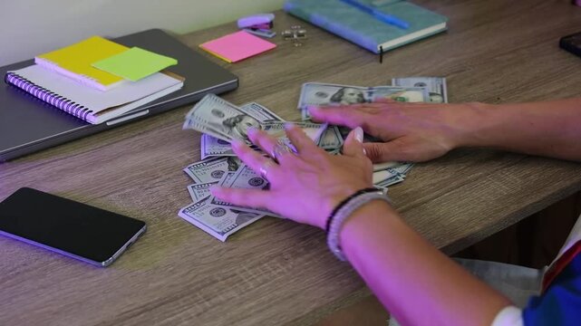Counting cash on a desk in a room with a phone and notebooks around
