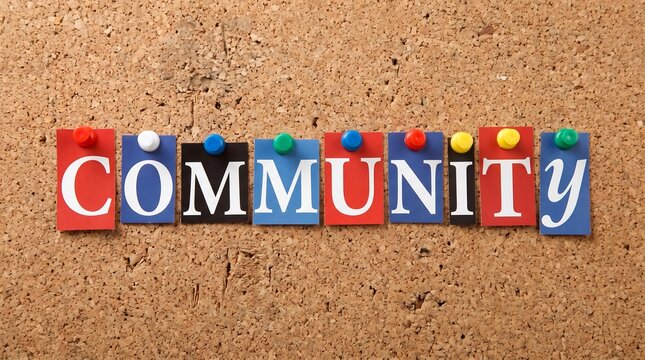 White letters spelling community on colorful rectangular paper pieces pinned to a textured brown cork board with small plastic pins
