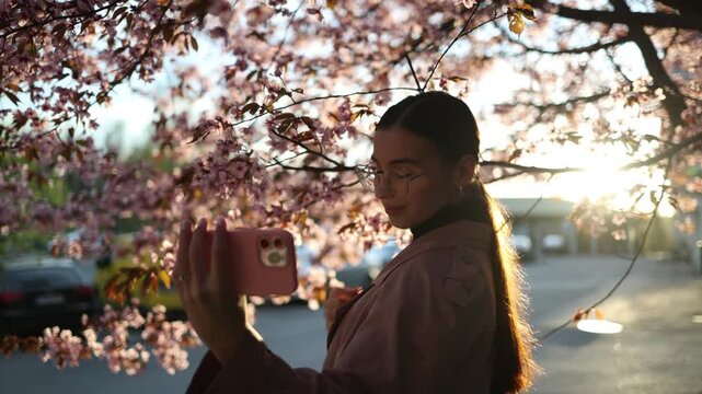 young woman taking selfies among blooming cherry blossom trees enjoying spring season and capturing memorable moments in a colorful park setting