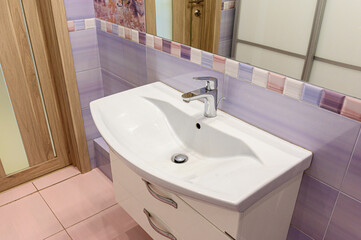 Fototapeta premium compact bathroom features white ceramic basin with curved design, chrome faucet, pastel purple tiles, decorative mosaic border, and white vanity with silver handles