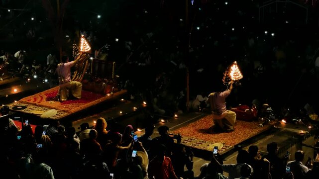 India, April 5, 2026 ceremony on the banks of the Ganges River in Varanasi. A back shot of a Pujari or Brahmin (Hindu Priest) holding fire lamps/ lantern/ Diyas Performing Ganga Pooja