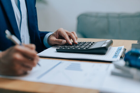Businessman using a calculator and writing on financial documents at desk for car insurance, vehicle loan accounting, and financial tax audit