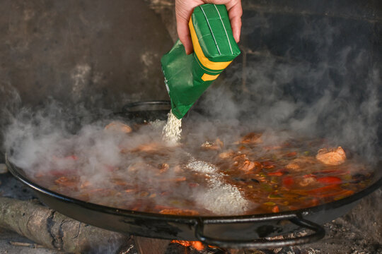 Man pouring rice into Valencian paella in wood fired oven