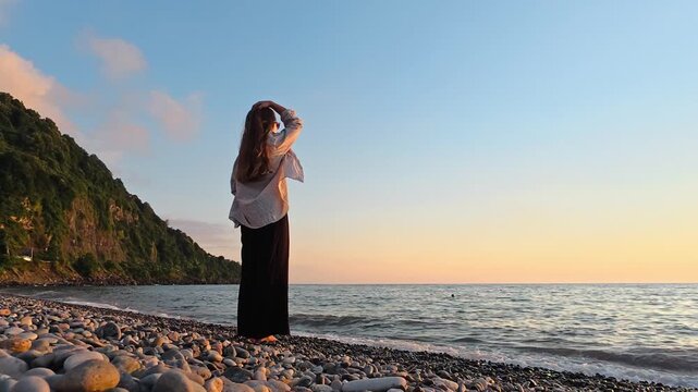 Woman standing on pebble beach at sunset and looking at the sea in Georgia