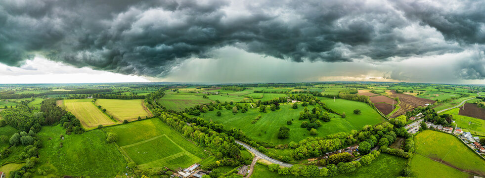 A powerful thunderstorm looms over expansive green fields in North Yorkshire with dark clouds swirling above the landscape under a moody sky