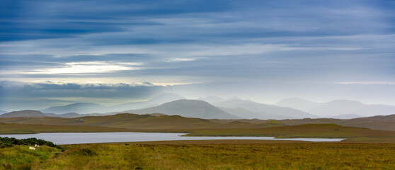 Fototapeta premium A calm evening view features rolling hills and a peaceful lake under an expansive sky with soft muted colors