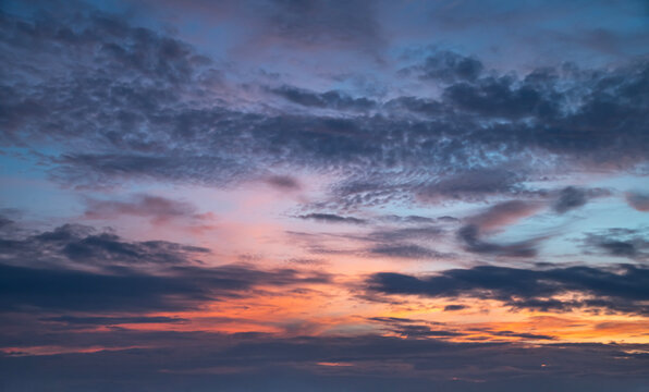 Vibrant Twilight Sky Background, Colorful Sunset Horizon with Layers of Dark Textured Clouds and Warm Orange Glow.