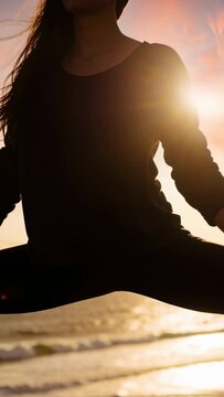 Vertical video: Sitting woman doing yoga on cliff as sun sinking beside sea in dark clothes