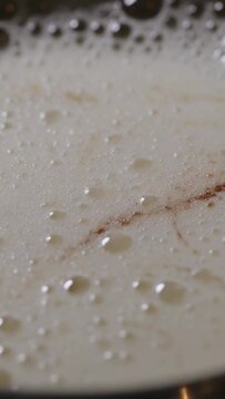 Vertical video: Foaming milk reacting to stovetop heat in pan, forming froth and brown swirls