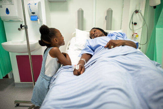Child visiting a patient in a hospital bed, both smiling warmly.