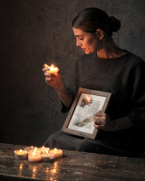 Grieving woman holding candle and old framed photograph in memory by candlelight