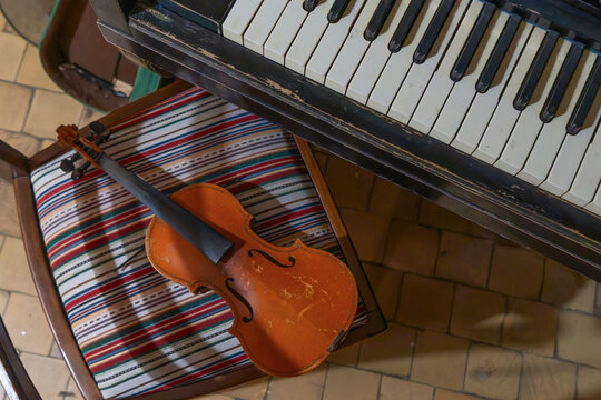 Vintage violin without strings resting on a retro striped chair next to an old piano keyboard, classic musical instruments in a nostalgic retro styled interior background
