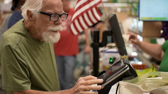 Senior man uses his credit card at the checkout counter in a grocery store during his shopping trip for food items