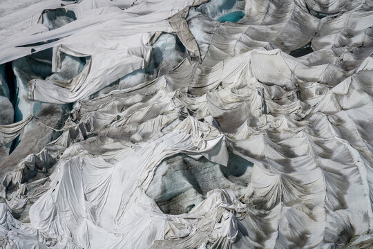 Aerial view of the Rhone Glacier covered with white protective blankets to reduce melting, showing the textured fabric draped over the glacial surface in Obergoms, Valais, Switzerland.
