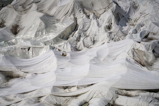 Aerial view of Rhone Glacier covered with white protective fleece to prevent melting, showing the textured fabric draped over the icy landscape in Obergoms, Valais, Switzerland.