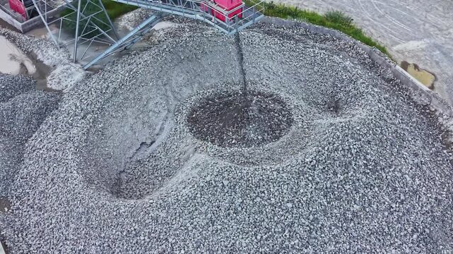 Aerial view gravel stockpile being formed as conveyor pours crushed stone into circular mound drone perspective reveals spiral pattern, gray texture,