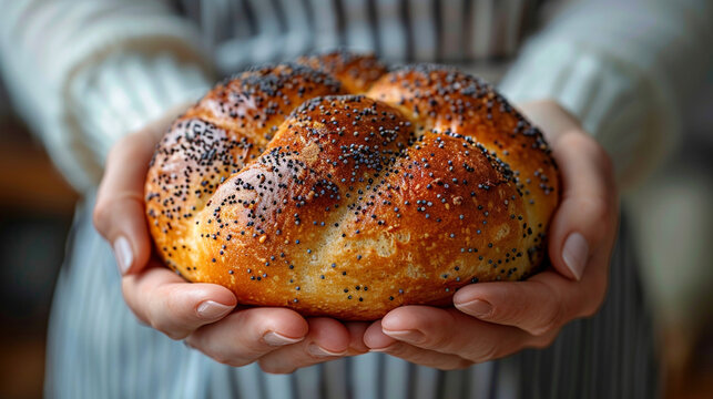 Baker hands holding a fresh golden brioche bun topped with poppy seeds in a rustic bakery, concept of traditional artisan baking.