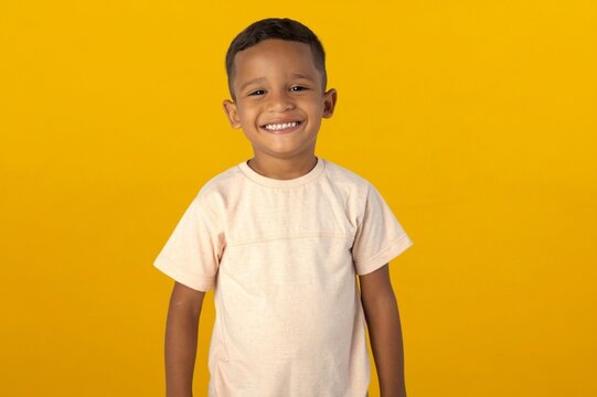 Cheerful young Latino boy smiling happily against a vibrant yellow studio background