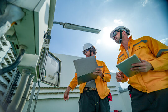 On-site view as a technician in an orange work jacket services telecom equipment on the building roof overlooking the city, capturing clean energy, solar power generation and engineering.