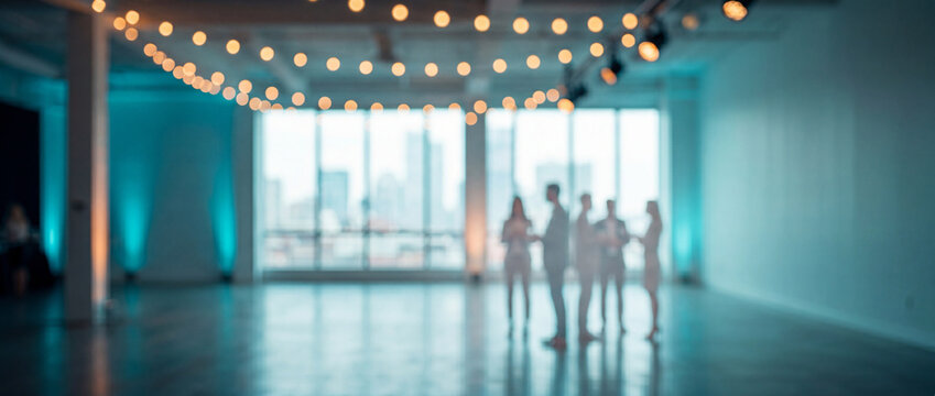 Blurred group of people in suits standing in a modern event space with string lights and city view through large windows, illuminated by blue uplighting