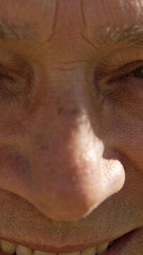 Vertical video: Smiling senior man squinting at sun in outdoor closeup, camera capturing face