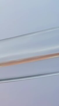 Vertical video: Glass arc sliding left in-studio at start over pale wall revealing filament, glints