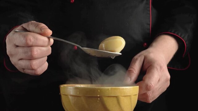 Chef hands in a black uniform stir a steaming bowl of soup, gradually transitioning to serving a portion with a spoon, highlighting the culinary process in a kitchen environment