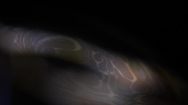 Abstract macro footage showing a subtle curved liquid film boundary. Low-key silver, bronze, and grey illumination highlights shifting organic interference lines and marbled textures fading