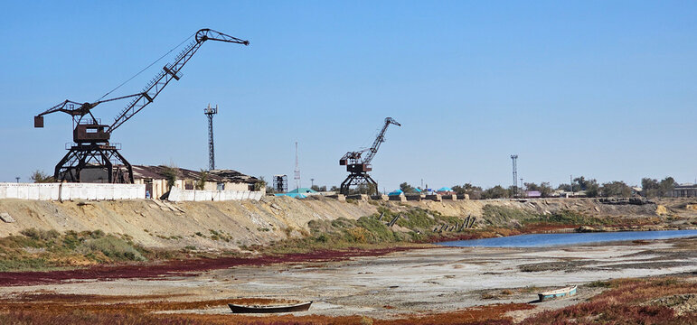 Former port cranes and abandoned boats on the exposed seabed near Aralsk, Kazakhstan. Documentary landscape illustrating the environmental consequences of the Aral Sea shrinkage.