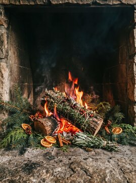 burning yule log decorated with evergreen branches, dried oranges and cinnamon in cozy stone fireplace. warm winter holiday atmosphere, christmas celebration. greeting card, festive background.
