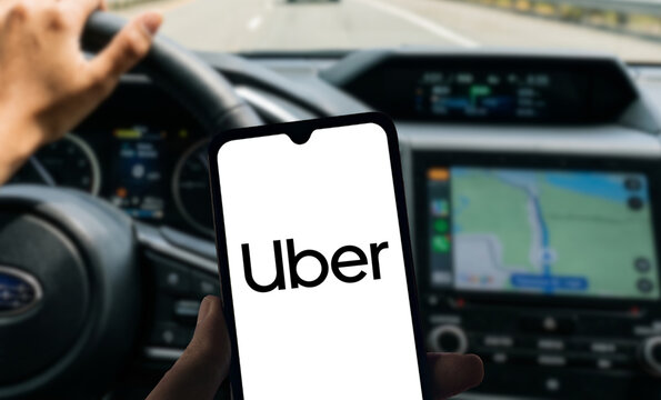 Hand Holding Smartphone with Uber Logo on Screen Inside a Car