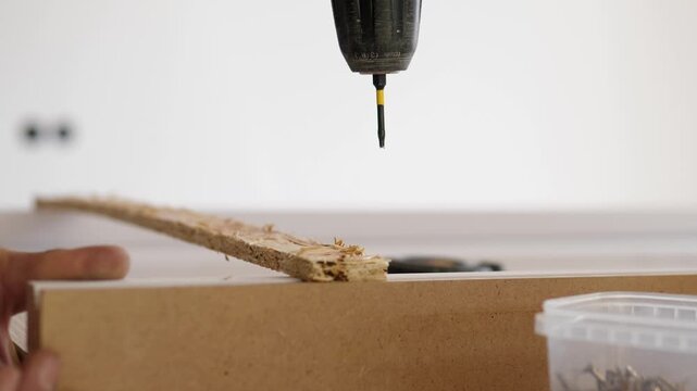 Across this short sequence, hand at upper center drives drill bit into rough cardboard edge on workbench, then steadily eases off near end, showing careful diy assembly, motion