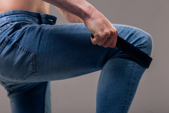 A muscular man in blue classic jeans with a bare torso is holding a belt. Concept: domination and play in a married couple, domestic violence, getting ready for work in the morning