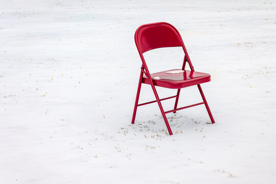 Red folding chair sitting in a snowy field, isolated and lonely