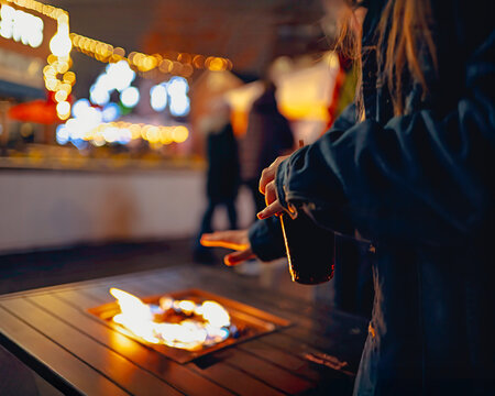 Girl warms her hand against a fire while holding a drink in a festive holiday atmosphere