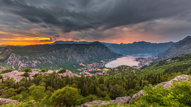 Aerial view of the Bay of Kotor at sunset with dramatic clouds over the surrounding mountains and lush green forests in Kotor, Kotor Municipality, Montenegro.