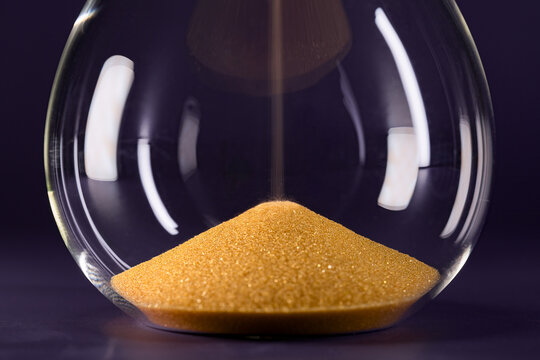 Close up of an hourglass with yellow sand isolated against a black background, symbolizing the passage of time