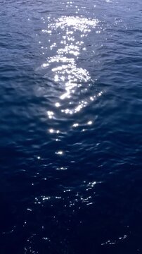 Calm ocean surface with bright sunlight reflecting across gentle waves, creating a shimmering path of light on the water