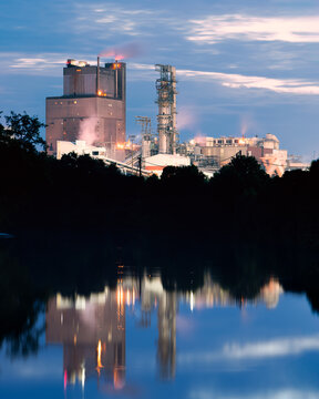 Dramatic gritty and industrial paper mill reflecting on a quiet lake at blue hour
