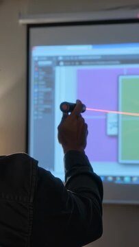 Vertical video: Raising red laser pointer, presenter in cap marking panels on screen, copy space