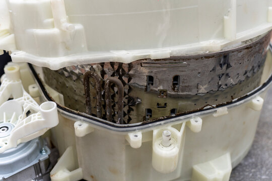 Close up of a dirty limescale covered heating element installed inside a disassembled washing machine stainless steel drum during appliance repair service.