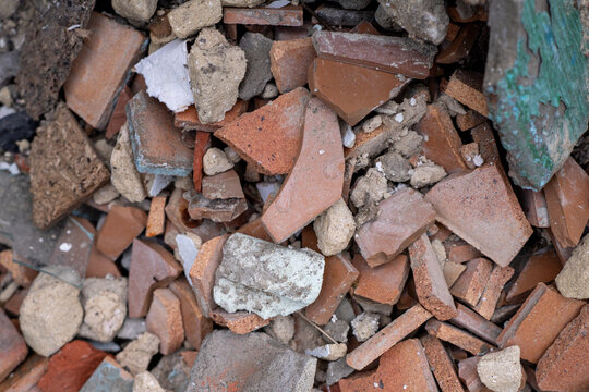 Top view of building demolition waste consisting of broken red brick pieces, crushed concrete blocks, and plaster debris at a construction site.