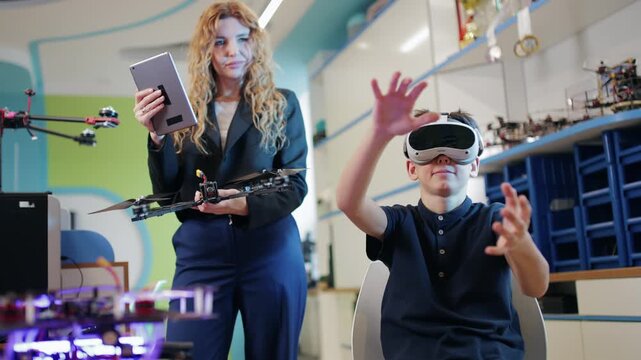 Tracking shot woman guiding boy controlling drone with vr headset and tablet in robotics lab workshop handheld pan movement.
