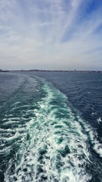 Scenic footage of a cruise ship sailing away across the open ocean, leaving behind visible ship tracks on the water surface.
