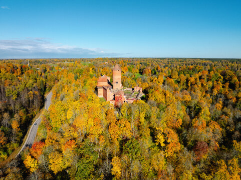 Aerial view of Turaida Castle surrounded by vibrant autumn forest with colorful fall foliage and a winding road in Sigulda, Siguldas novads, Latvia.