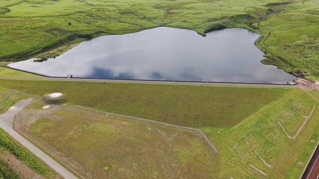 Scenic drone perspective of a grassy dam wall and reflective water reservoir