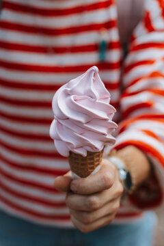 Person holding a pink soft-serve ice cream cone in a striped top.