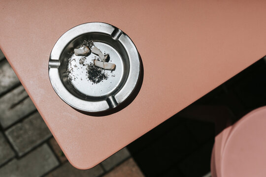 Metal ashtray with cigarette butts on a peach-colored table